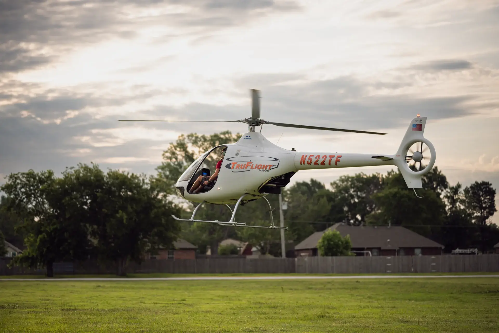 Helicopter flying over a grass field seen from the back